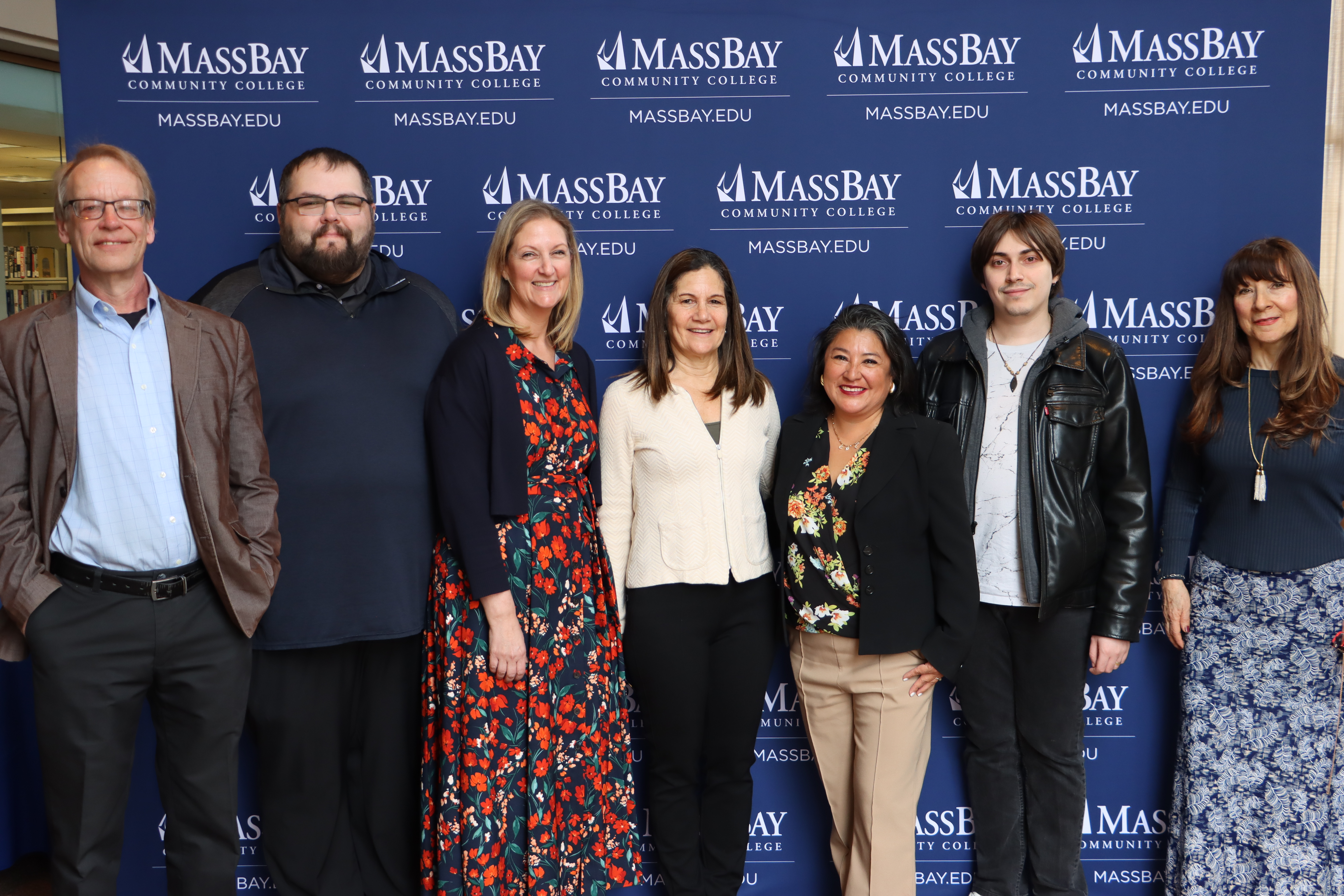 Seven members of the Admissions Team smile for the camera, with a MassBay step-and-repeat as a backdrop.