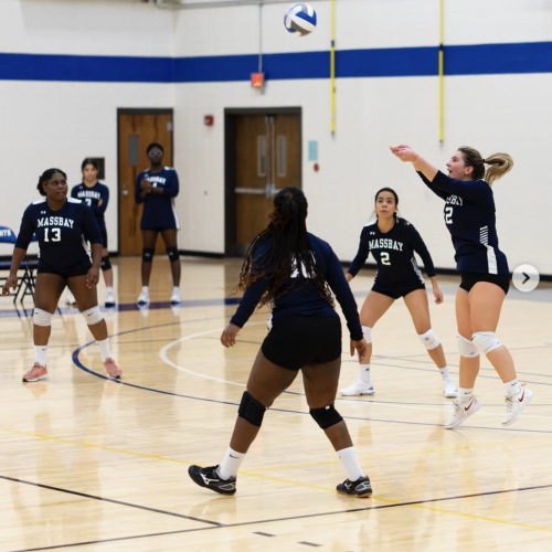 Member of the MassBay women's volleyball team bumps the ball while three of her teammates watch carefully.