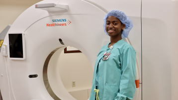Smiling sonography student in scrubs standing next to an imaging machine